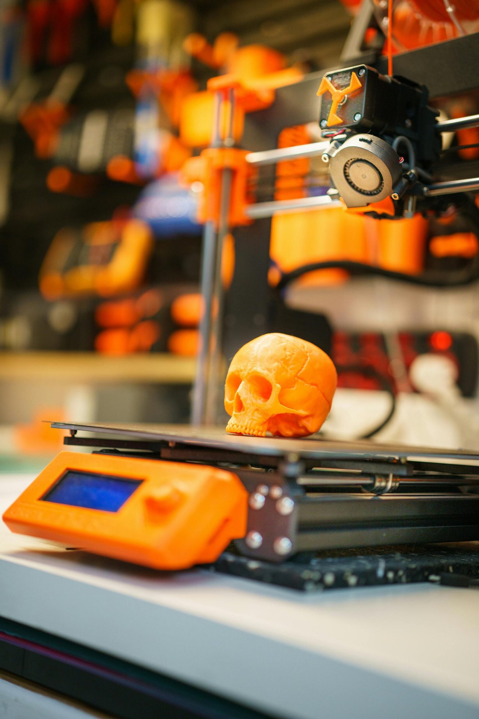 A close-up of an orange 3D printed skull on a 3D printer, showcasing modern technology in a workshop setting.