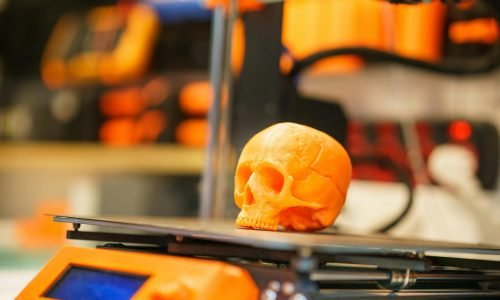 A close-up of an orange 3D printed skull on a 3D printer, showcasing modern technology in a workshop setting.